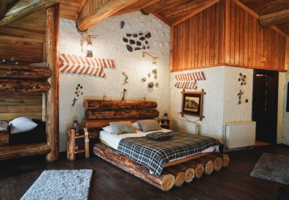 Interior primitor de pensiune montană, cu mobilier din lemn, textile tradiționale și fereastră spre brazi